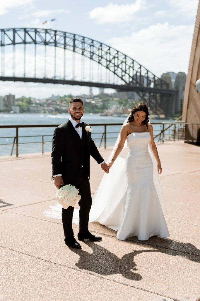 bride and groom walking infront of harbour bridge with reflection