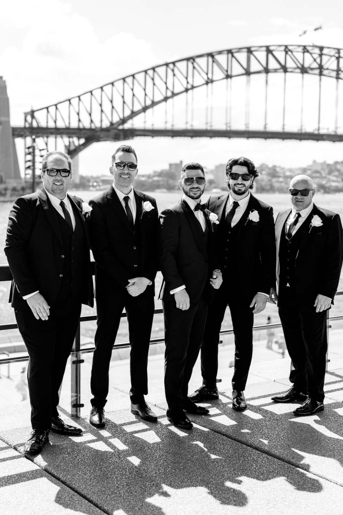 groomsman smiling infront of harbour bridge black and white