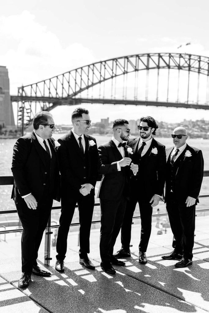 groomsman smiling infront of harbour bridge black and white