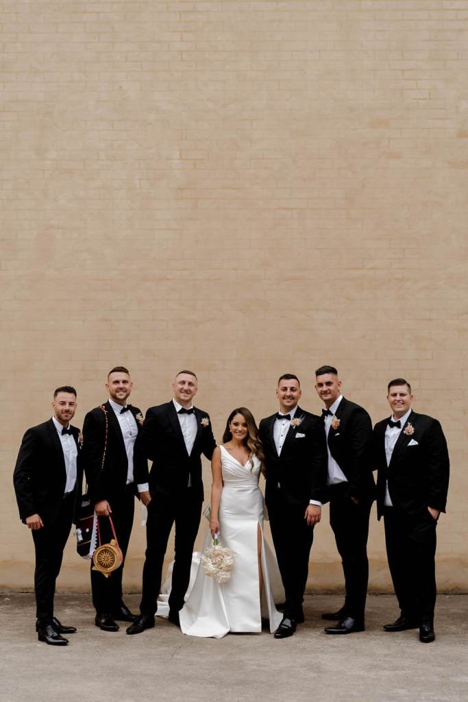 Groomsman and bride smiling on brick wall
