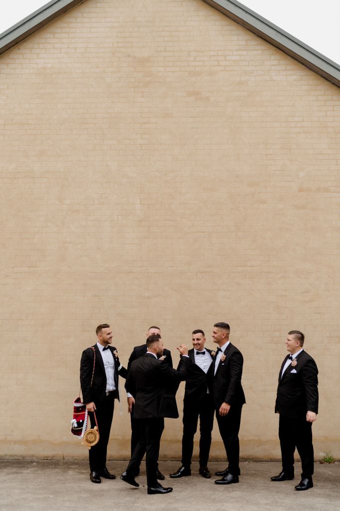 Groomsman smiling on brick wall