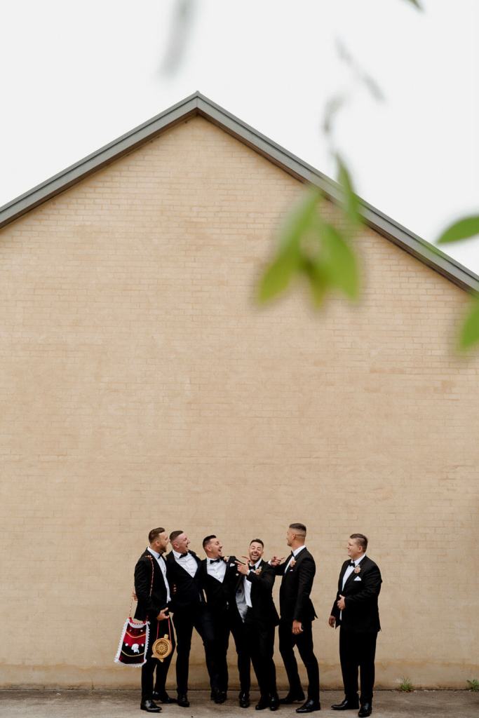 Groomsman smiling on brick wall